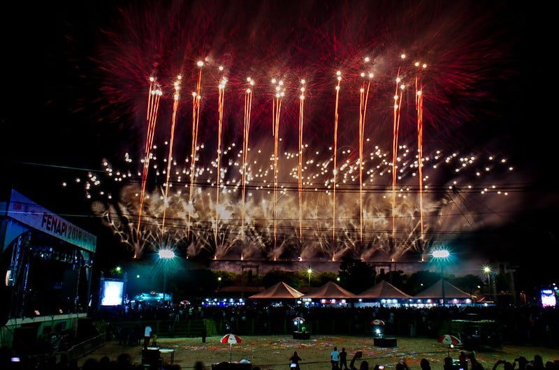 Show de fogos de artifício iluminando o céu durante a comemoração dos 150 anos de Santo Antônio do Monte, com várias explosões de cores e fumaça, e uma multidão reunida embaixo.