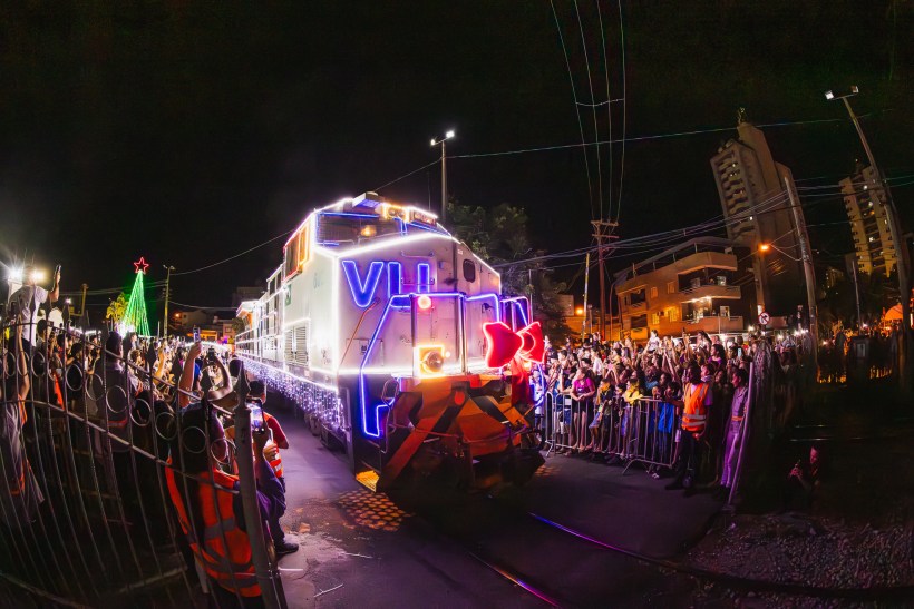 Locomotiva iluminada decorada para o Natal, passando por multidão animada em um evento festivo à noite.