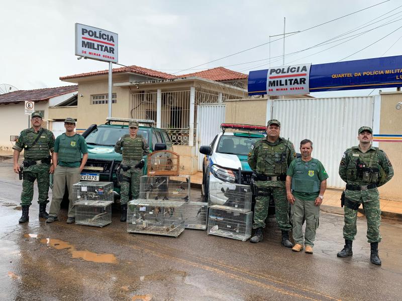 Agentes da Polícia Militar de Meio Ambiente posam em frente ao quartel, com veículos e gaiolas apreendidas durante operação para combate ao tráfico de aves silvestres.