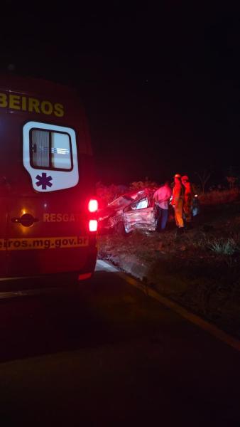 Ambulance and emergency personnel responding to a car accident at night with a damaged vehicle on the roadside.
