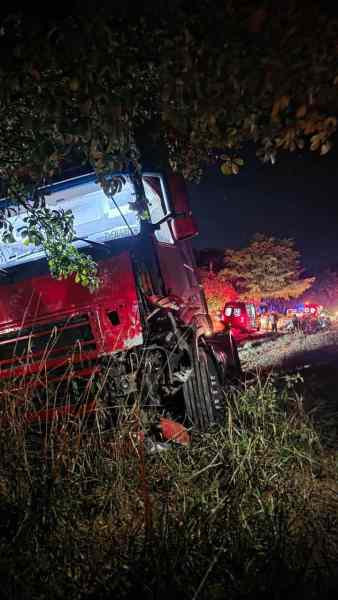 A red truck leaning to one side in a grassy area, illuminated by nearby lights at night.