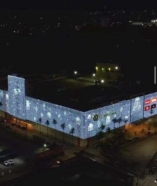 Fachada de um shopping decorada com luzes natalinas, iluminada à noite, exibindo adornos festivos no estilo de inverno.