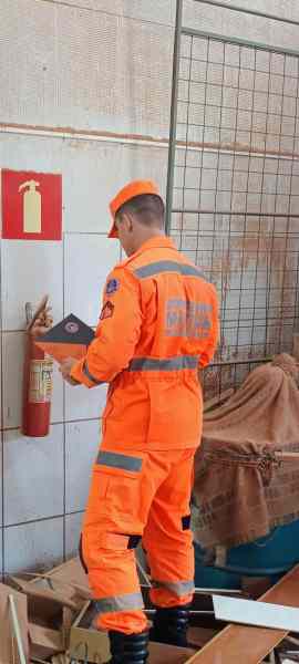 Bombeiro militar inspecionando uma edificação, utilizando um tablet e ao lado de um extintor de incêndio, durante a 4ª Operação Alerta Vermelho 2025.