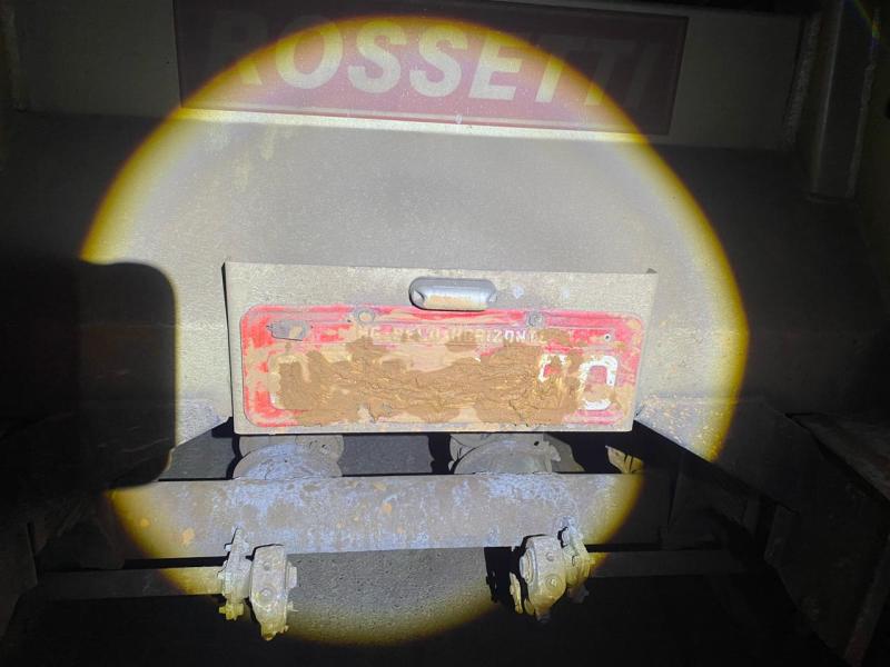 Placa de veículo coberta com barro, dificultando a identificação, iluminada por um foco de luz.