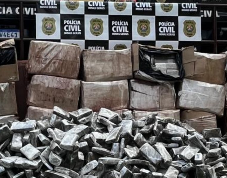 Montanhas de pacotes de maconha apreendidos pela Polícia Civil de Minas Gerais, com um fundo exibindo a bandeira da instituição.