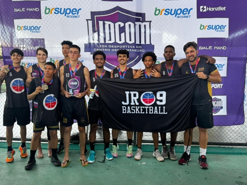 Equipe JR09 Basketball segurando um banner e troféus após vencer a Liga Desportiva Centro-Oeste Mineiro, com jogadores e um treinador sorrindo em evidência.