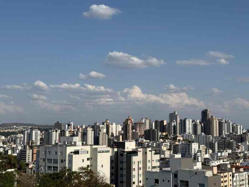 Vista panorâmica de um bairro urbano com prédios altos e céu azul com nuvens brancas.