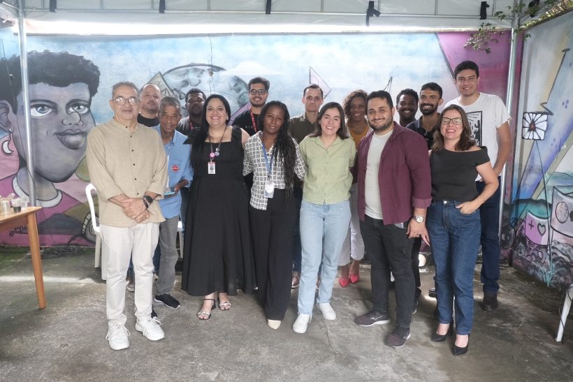 Grupo de pessoas posando para uma foto em frente a um mural colorido com arte urbana.
