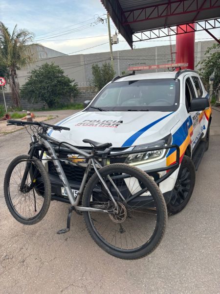 Viatura da Polícia Militar com uma bicicleta apreendida na frente, em um ambiente urbano.