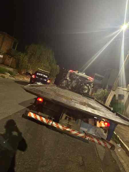 Uma motocicleta sendo rebocada por um guincho em uma rua à noite, com iluminação urbana visível ao fundo.