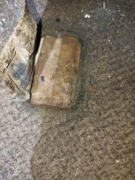 Um bloco de cimento ou material similar mostrado em um tapete de carro sujo, próximo a um pedaço de revestimento rasgado.