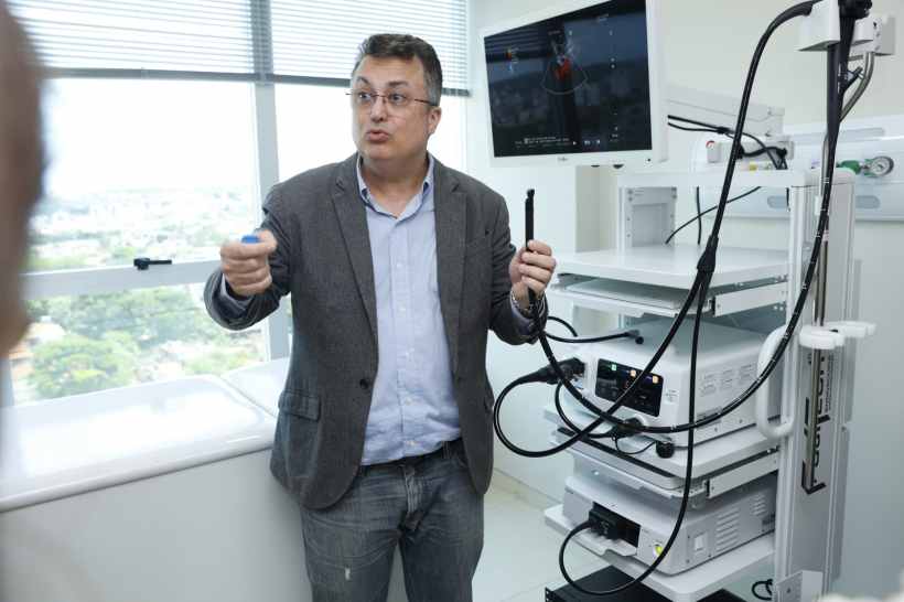 Médico apresentando equipamento de endoscopia em sala moderna, com tela ao fundo mostrando imagens de ultrassonografia.