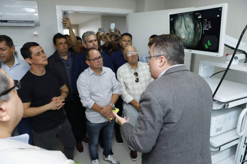 A inauguração do Serviço de Endoscopia e Colonoscopia é apresentada em uma sala, com um grupo de pessoas assistindo a uma demonstração de um aparelho avançado e uma tela mostrando imagens médicas.
