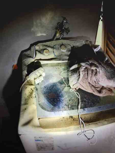 Close-up of a soiled washing machine in a fire-damaged residence, showing dirt and debris.