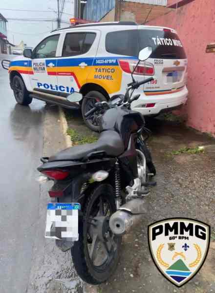 Imagem de uma motocicleta preta estacionada ao lado de um veículo da Polícia Militar com identificação de Tático Móvel, em um ambiente urbano.