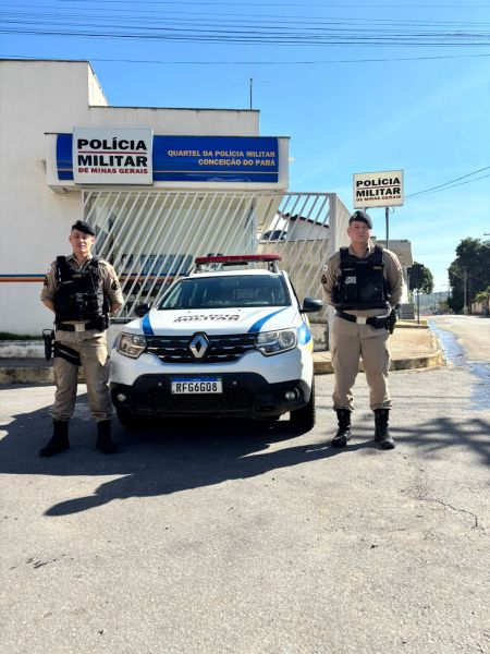 Dois policiais militares em frente ao Quartel da Polícia Militar de Minas Gerais, em Conceição do Pará, ao lado de um veículo oficial da corporação.