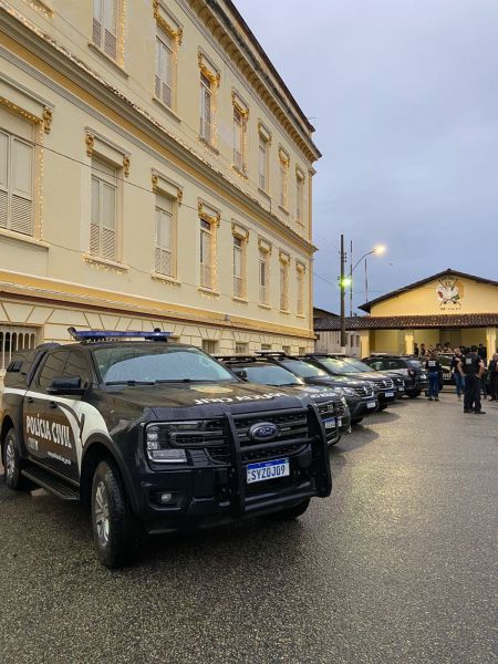 Veículo da Polícia Civil estacionado em frente a um prédio, com agentes de segurança em atividade.
