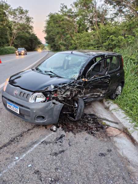A damaged black car is parked on the side of a road, showing significant front-end damage and leaking fluids.