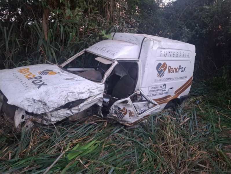 Um veículo funerário danificado estacionado em uma área com grama alta.