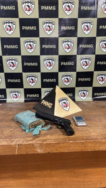 Um revólver, uma balança de precisão e um tablete de maconha dispostos sobre uma mesa, com um fundo feito de painéis da Polícia Militar de Minas Gerais.