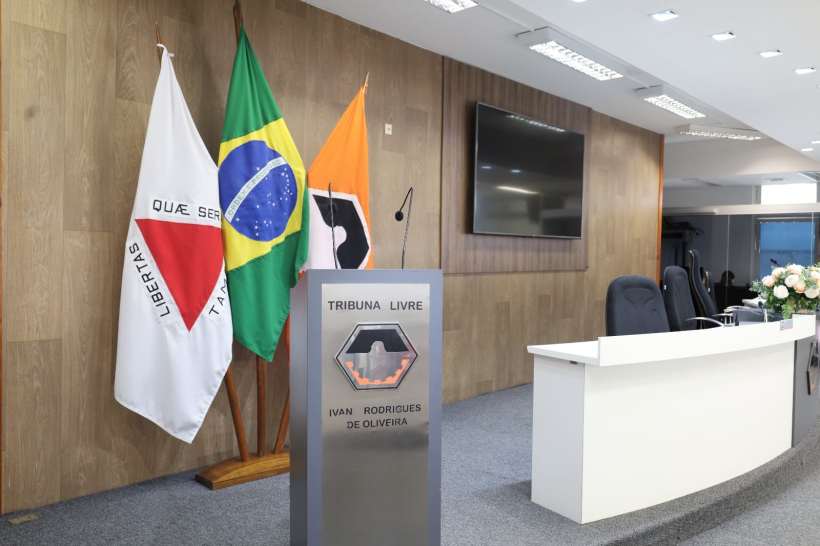 Interior da sala da Tribuna Livre 'Ivan Rodrigues de Oliveira', com bandeiras brasileiras e um espaço preparado para manifestações cidadãs.