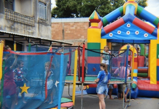 Crianças brincando em um pula-pula colorido e trampolins, em um evento festivo ao ar livre.