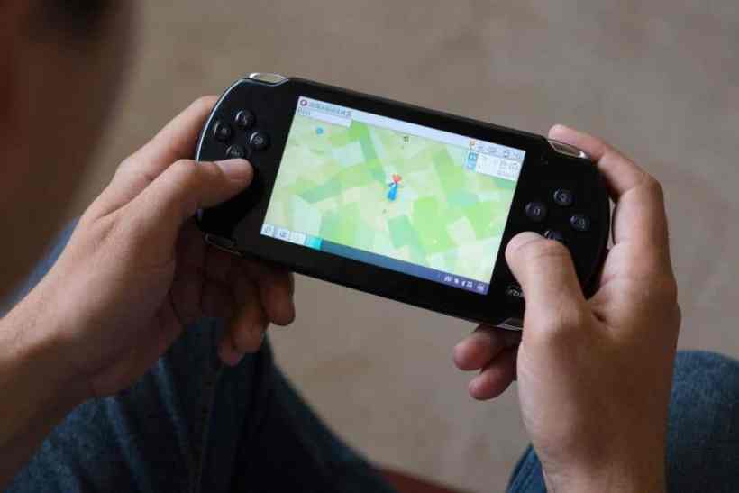 Um jogador segurando um console portátil, exibindo um mapa na tela enquanto joga.