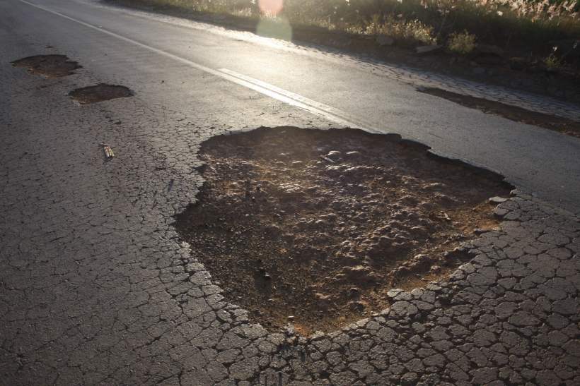 Buracos grandes em uma estrada asfaltada, com a superfície ao redor danificada pela erosão.