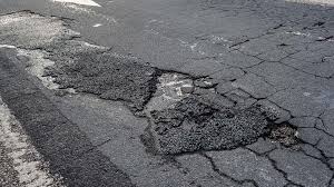 Trecho de estrada com buracos e asfalto deteriorado.