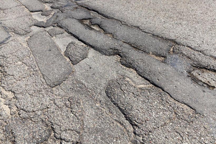 Asfalto danificado com fendas e buracos visíveis.