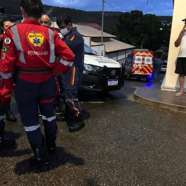 Equipe de resgate reunida em uma rua, com ambulâncias ao fundo e uma pessoa observando ao lado.