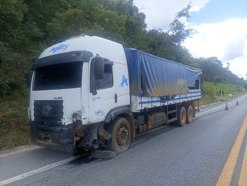 Caminhão com danos estendido na beira da estrada, com carregamento coberto por uma lona azul.