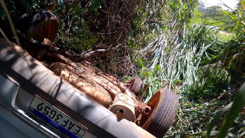 Um carro capotado em um local coberto de vegetação, com as rodas visíveis e parte da estrutura exposta.
