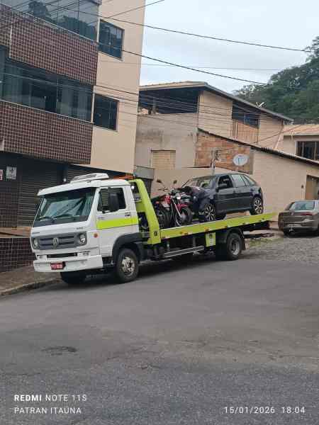 Caminhão guincho transportando um carro e duas motocicletas em uma rua urbana.