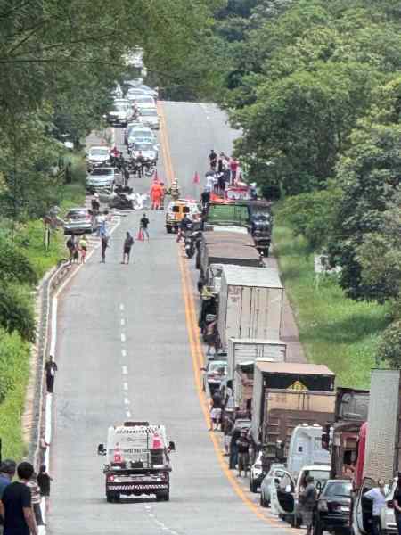 Caminhão estacionado em uma rodovia com vários veículos parados e pessoas caminhando ao longo da estrada, rodeados por vegetação.