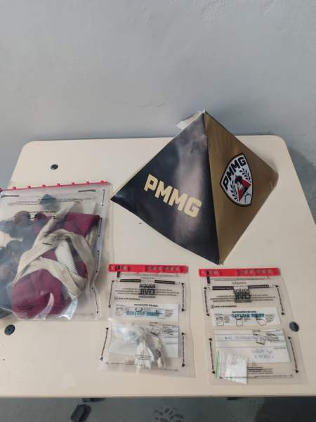 Objeto triangular com o logotipo da PMMG, ao lado de sacolas plásticas contendo materiais variados e documentos.