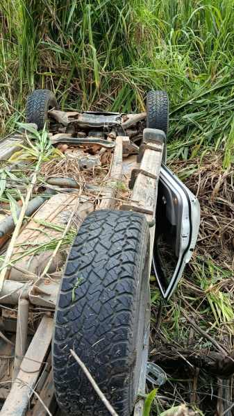 Veículo capotado em área de vegetação densa, mostrando o interior do carro e pneus.