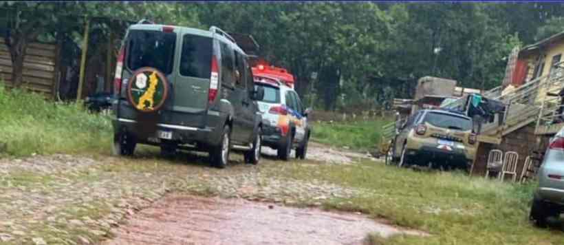 Vários veículos estacionados em uma rua de paralelepípedos, rodeados por um ambiente verde e com vegetação ao fundo.