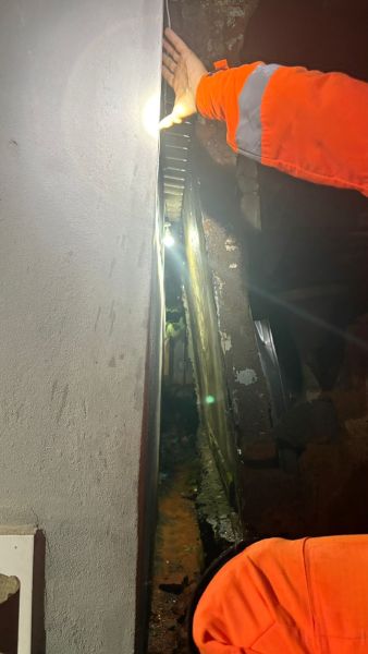 Imagem mostrando uma mão segurando uma lanterna ao longo de uma fenda estreita entre duas paredes, com iluminação destacando o espaço interno.