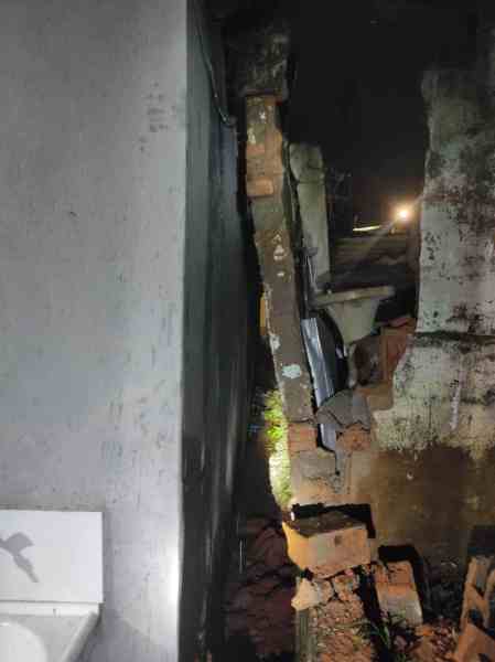 Imagem de uma parede danificada à noite, com tijolos expostos e uma estrutura de alvenaria quebrada ao lado.