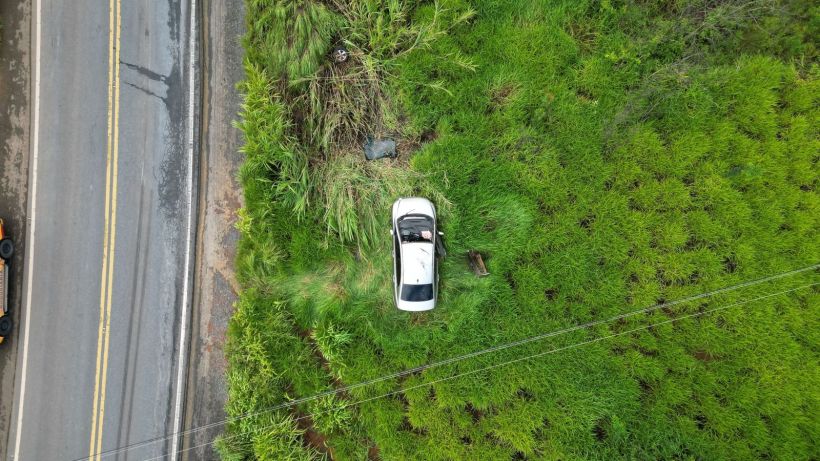 Vista aérea de um carro branco parado em um campo verde ao lado de uma estrada.