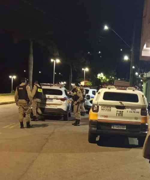 Policiais militares em patrulha à noite, abordando veículos em uma rua iluminada.