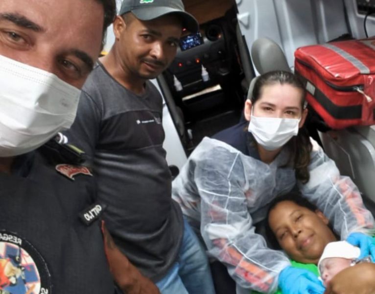 Quatro pessoas em uma ambulância, incluindo um paramédico e uma mulher segurando um bebê recém-nascido, todos usando máscaras de proteção.