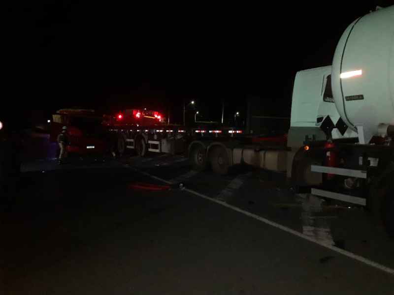 Acidente de trânsito à noite envolvendo caminhões na estrada, com veículos danificados e luzes de alerta visíveis ao fundo.