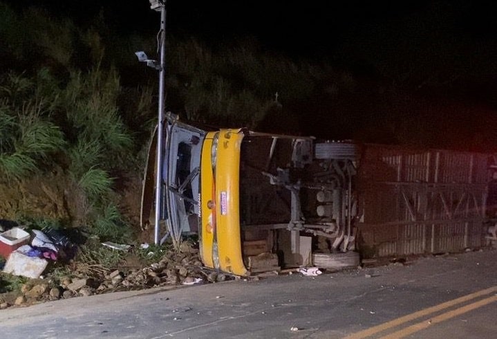 Um caminhão tombado na beira da estrada durante a noite, com objetos espalhados ao redor.