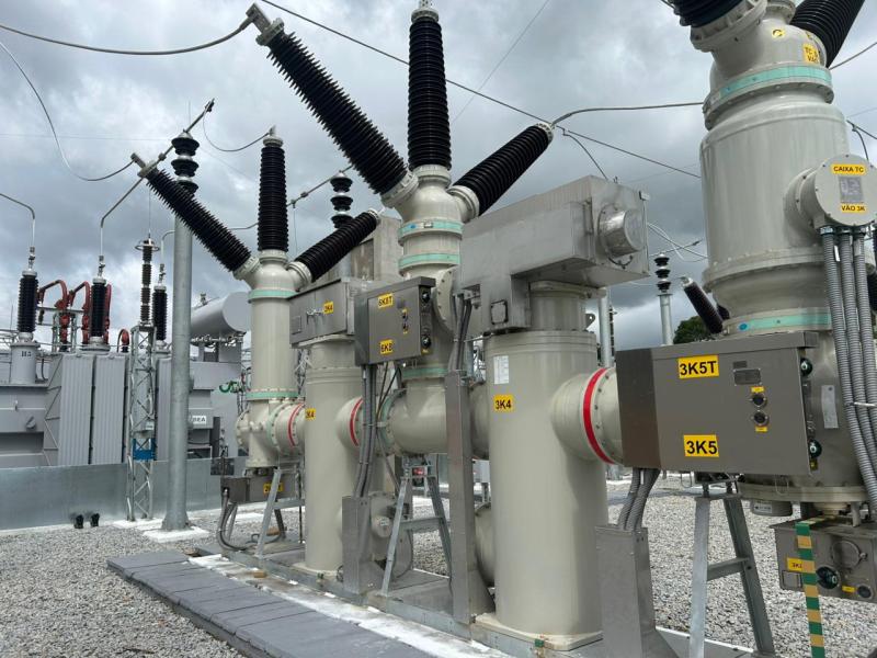 Equipamentos elétricos em uma subestação, com estruturas metálicas e isoladores, sob um céu nublado.