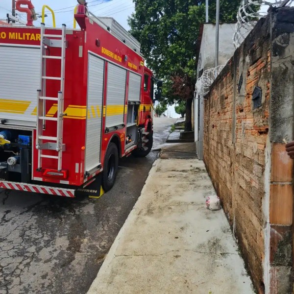 Caminho com caminhão de bombeiros estacionado, cercado por muro de tijolos e calçamento; árvores ao fundo.