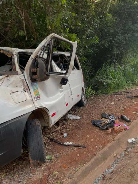 Furgão danificado abandonado ao lado da estrada, com a porta da frente aberta e alguns objetos pessoais ao redor.
