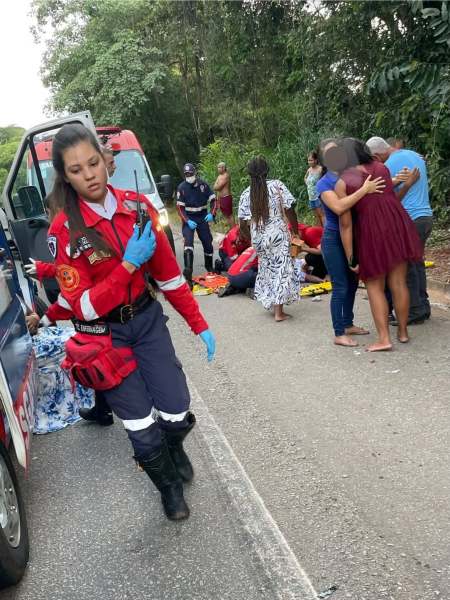 Uma equipe de emergência se mobiliza em uma cena de acidente na estrada, com um socorrista em uniforme vermelho e azul, prestando assistência a vítimas ao lado de um veículo de resgate.
