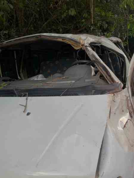 Carro acidentado com teto danificado e vegetação ao fundo.